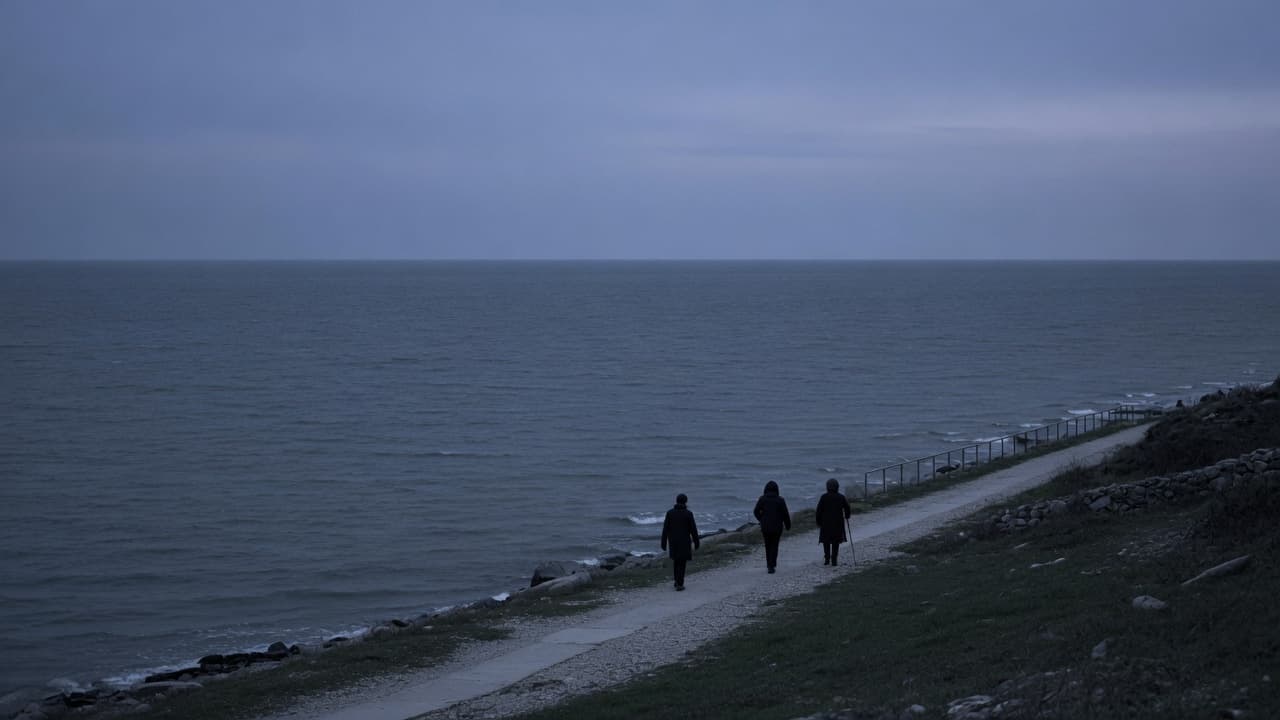Three people walking away along a coastal path at dusk.
